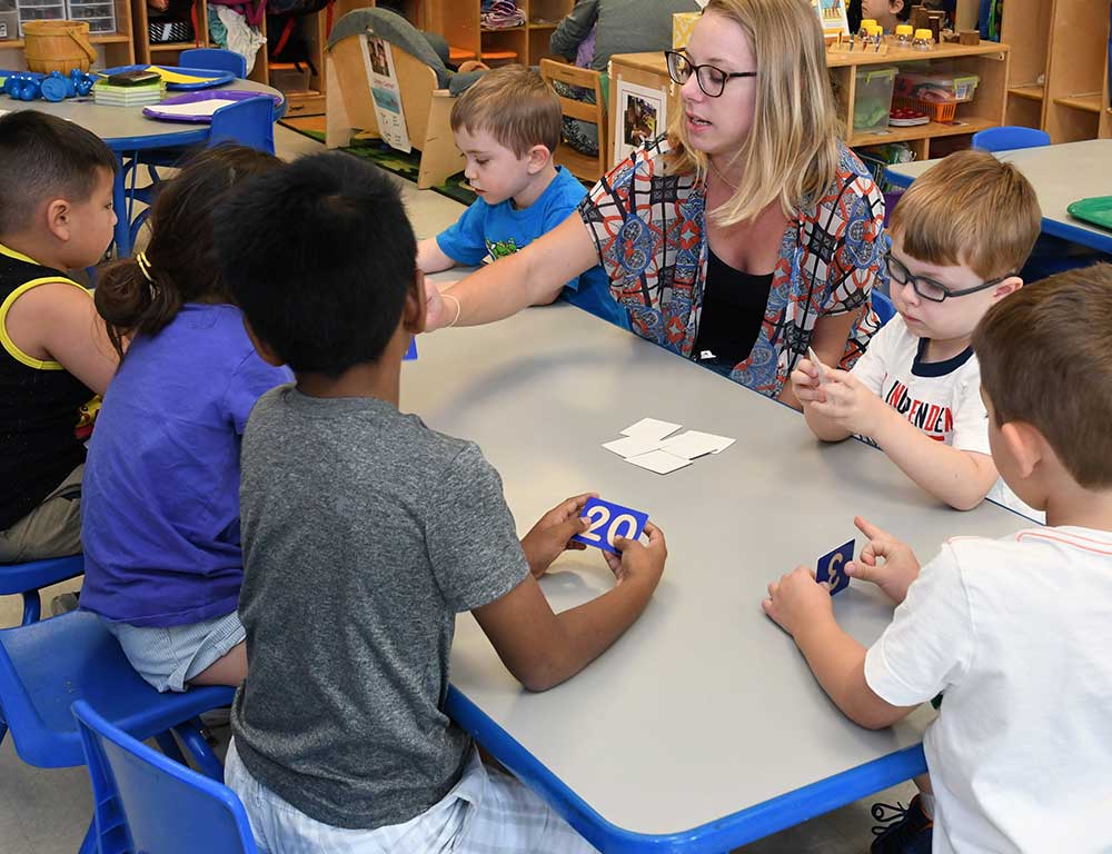 Teacher and children sitting at a table working on a learning activity