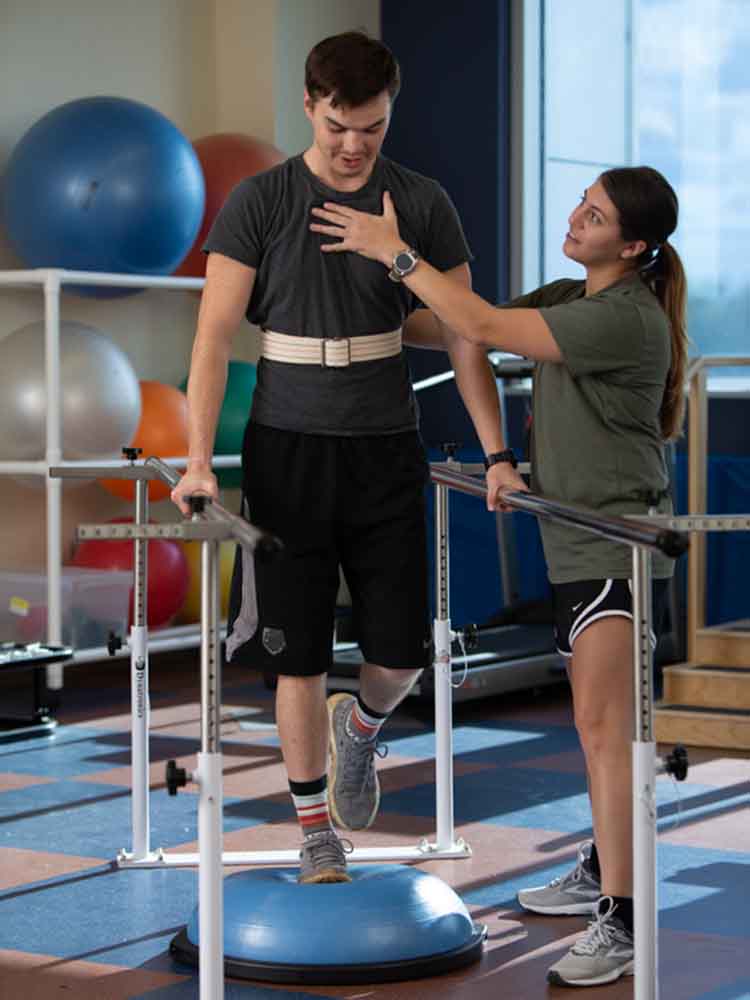 pta helping patient maintain balance while he is on bosu ball and holding bars