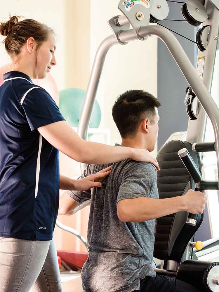 pta helping patient complete an exercise on an excercise machine